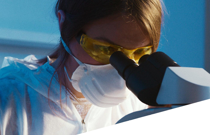 A woman wearing safety glasses is looking into a microscope