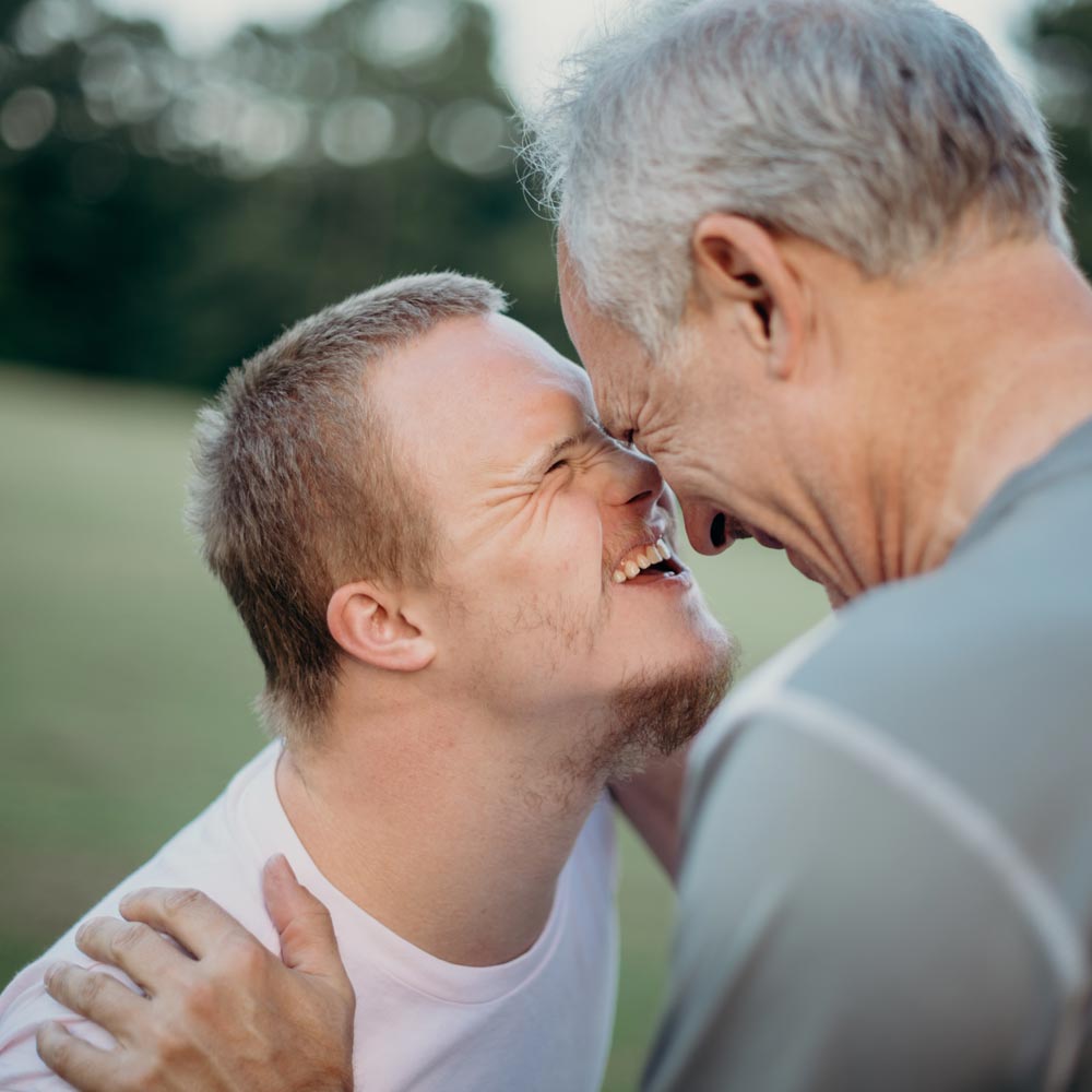 A young man and older man touching noses in the park