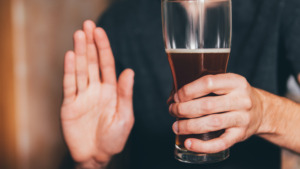A man holding a glass of beer and he is giving a hand gesture saying "stop