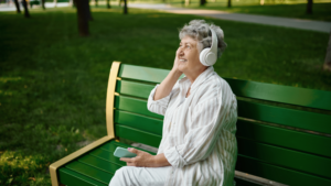 an elderly lady sitting on a park bench listening to music on her smartphone device with headphones