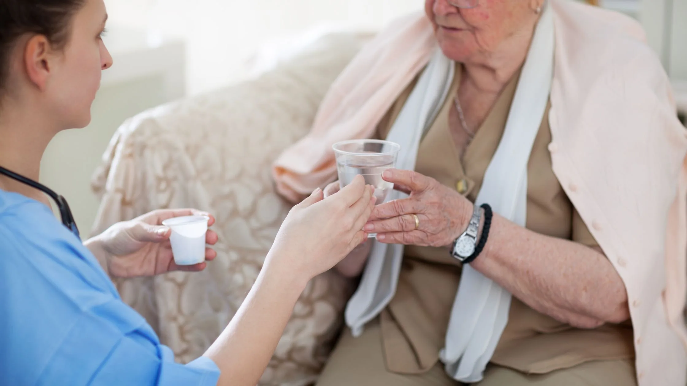 a nurse handing a cup of water to a patient while sitting down
